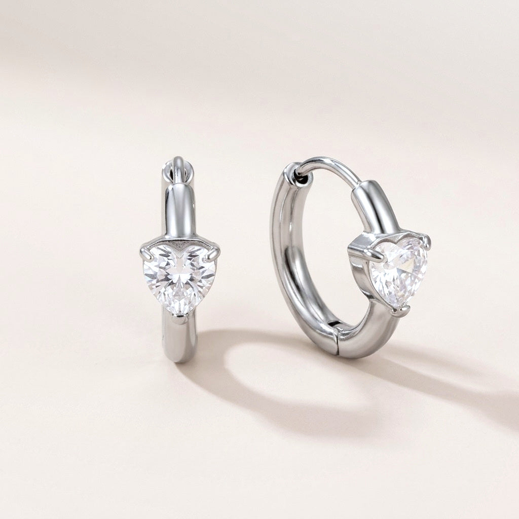 Sweetheart Spark Huggies Silver: hypoallergenic huggie hoop earrings, shown front and side on a soft stone background