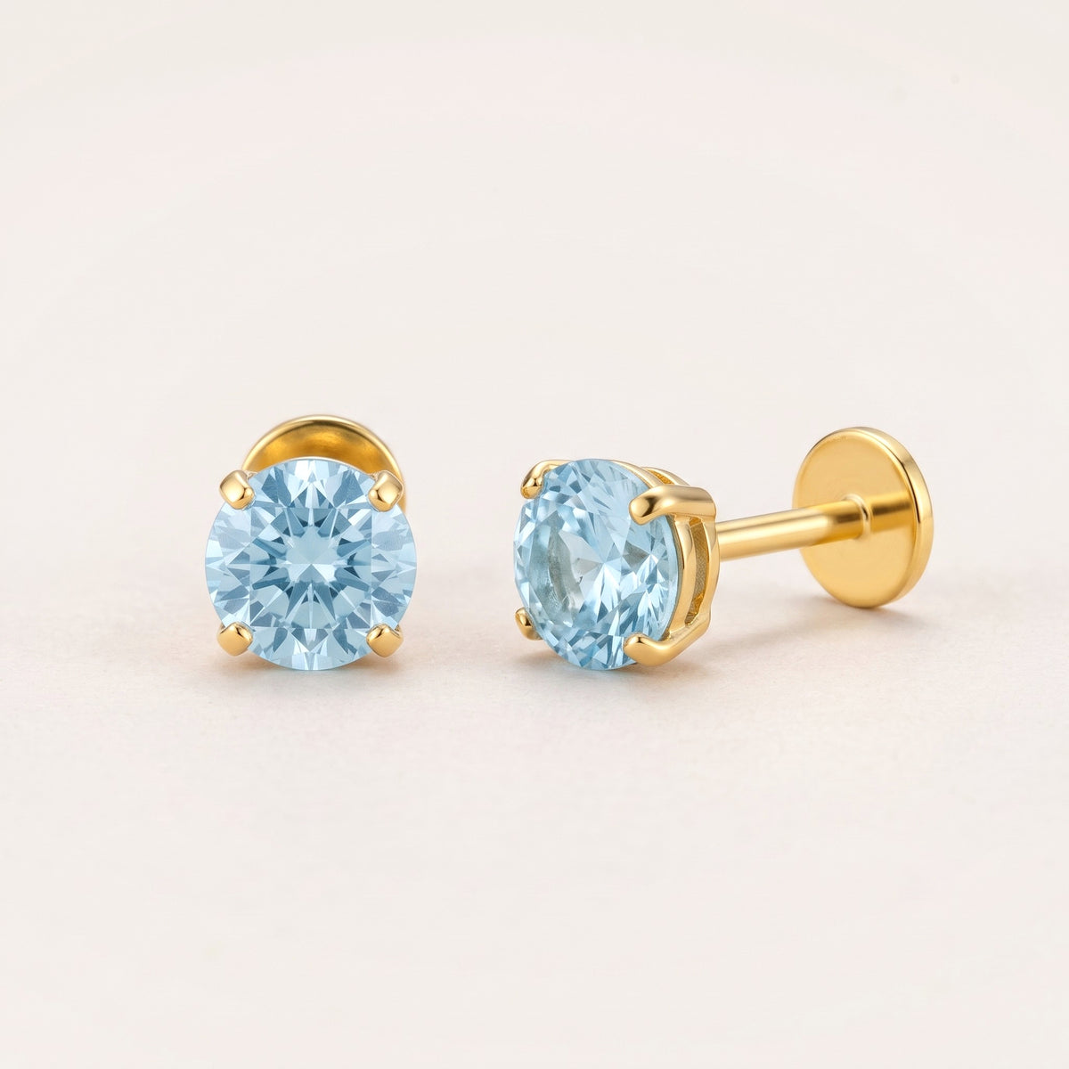 The Birthstone Flat Back Studs Gold in Aquamarine: hypoallergenic kids' flat back stud earrings, shown front and side on a soft stone background