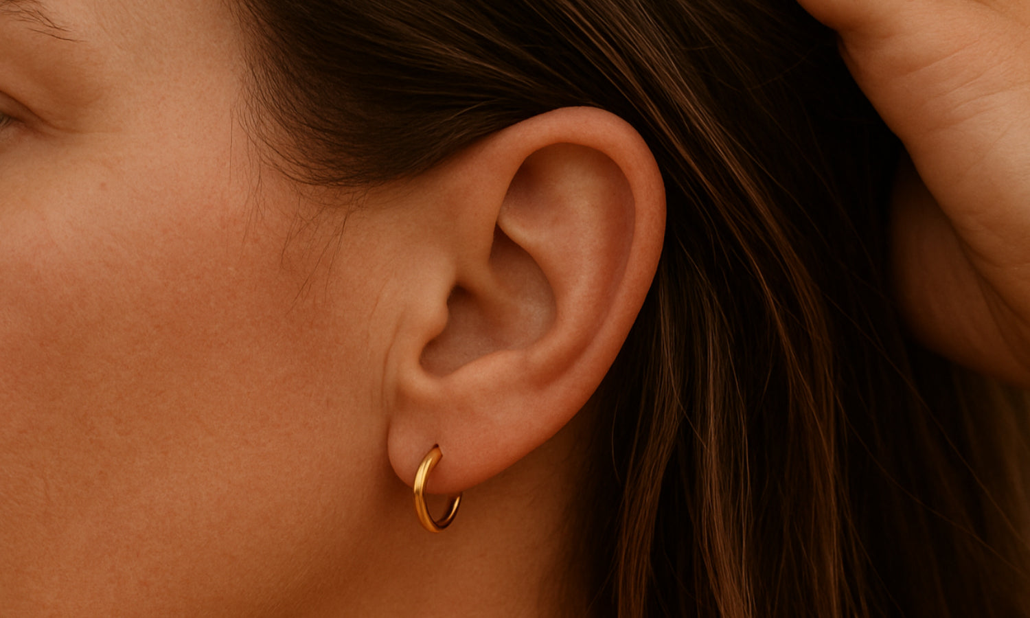 Close-up of an ear with a gold hoop earring on a warm-toned background