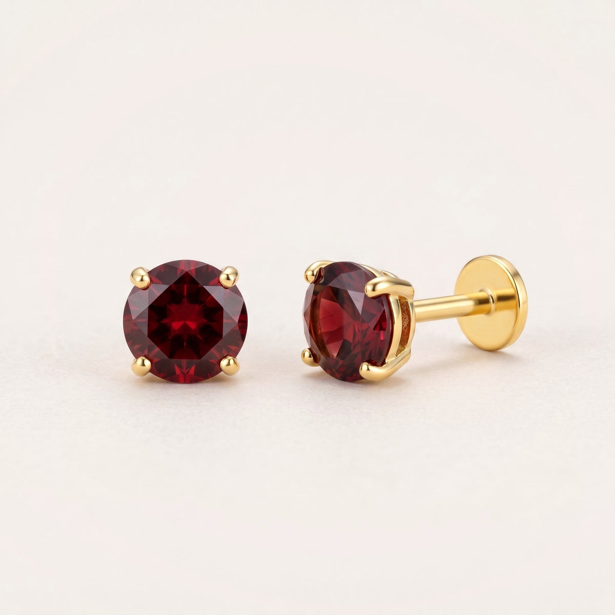 The Birthstone Flat Back Studs Gold in Garnet: hypoallergenic kids' flat back stud earrings, shown front and side on a soft stone background