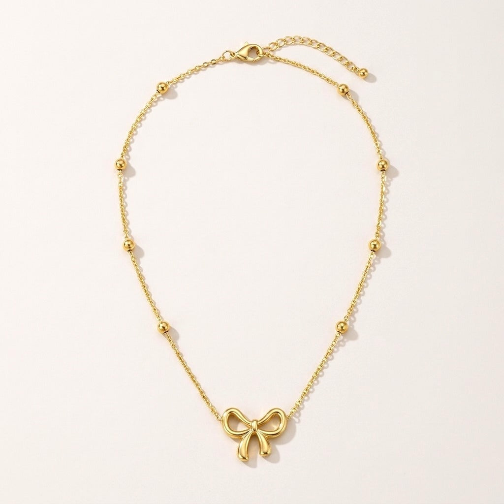 Gold Bow Necklace: hypoallergenic kids' necklace, laid flat on a soft stone background